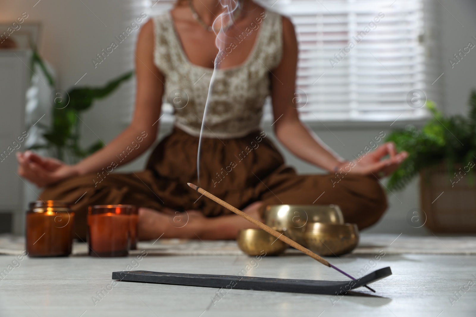 Photo of Young woman practicing yoga on floor indoors, focus on smoldering incense stick