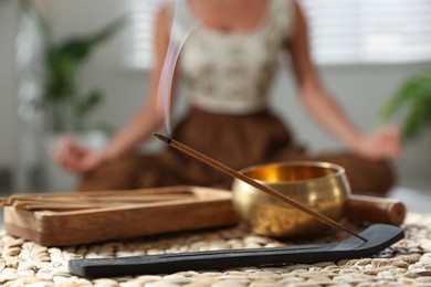 Photo of Incense stick smoldering in holder and tibetan singing bowl indoors, selective focus