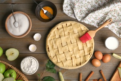 Photo of Uncooked homemade apple pie and ingredients on wooden table, flat lay