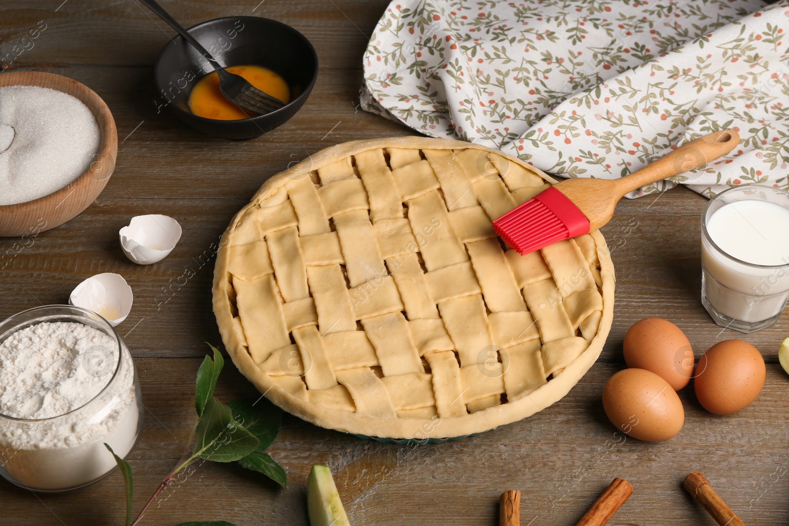 Photo of Uncooked homemade apple pie and ingredients on wooden table