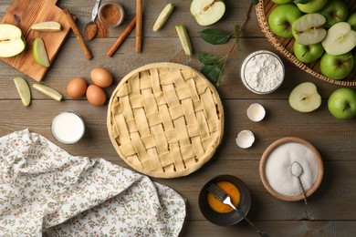 Photo of Uncooked homemade apple pie and ingredients on wooden table, flat lay