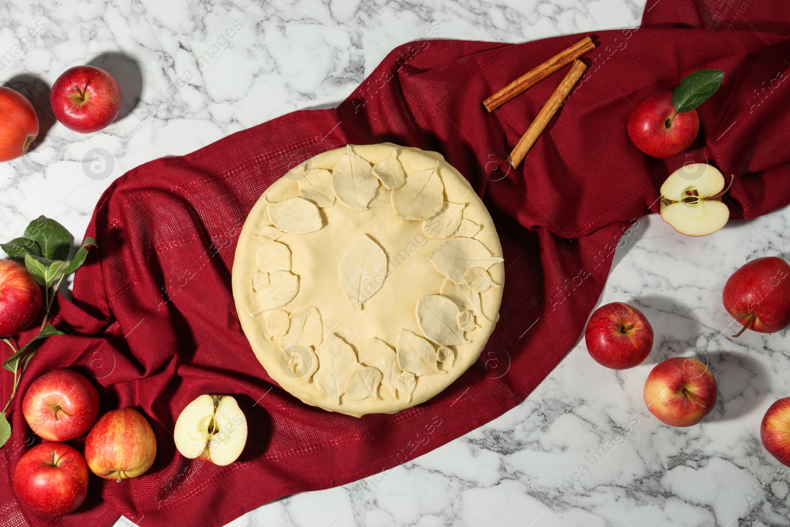 Photo of Raw homemade pie, apples and cinnamon sticks on white marble table, flat lay