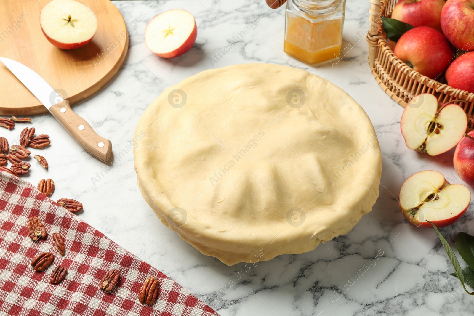 Photo of Raw homemade apple pie and ingredients on white marble table