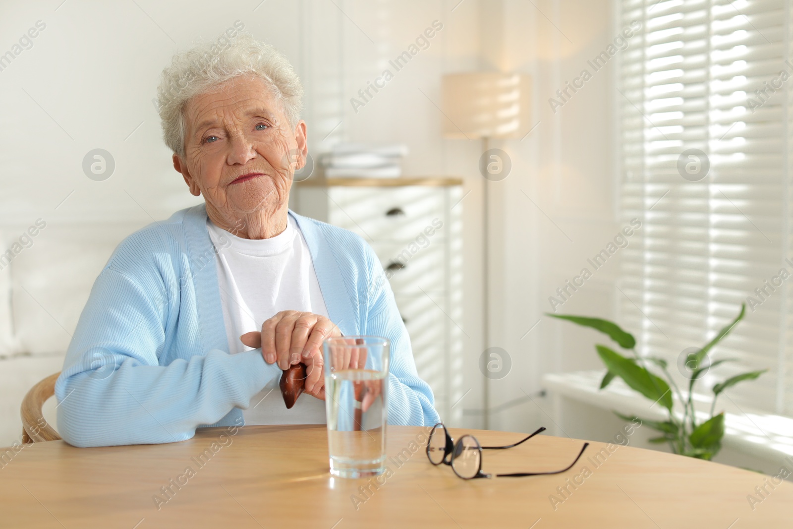 Photo of Thoughtful senior woman feeling lonely at table with glass of water indoors