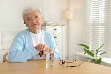 Photo of Thoughtful senior woman feeling lonely at table with glass of water indoors