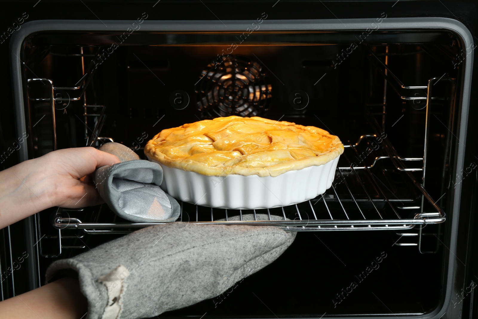 Photo of Woman putting homemade apple pie into oven in kitchen, closeup