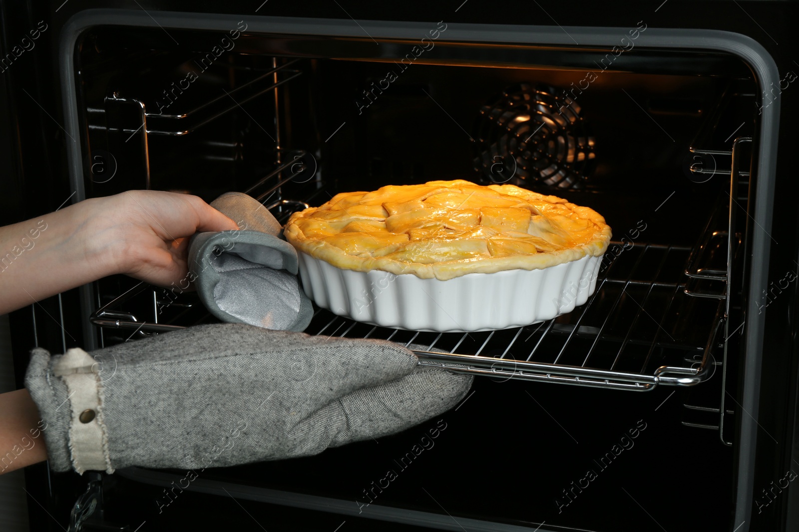 Photo of Woman putting homemade apple pie into oven in kitchen, closeup