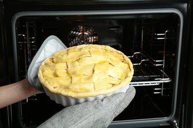 Photo of Woman putting homemade apple pie into oven in kitchen, closeup