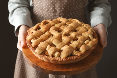 Photo of Woman holding wooden board with tasty homemade apple pie on black background, closeup