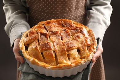 Photo of Woman holding tasty homemade apple pie on dark background, closeup