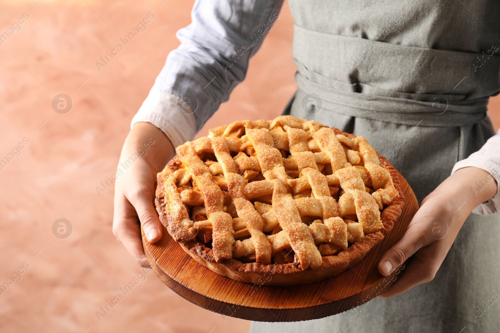 Photo of Woman holding wooden board with tasty homemade apple pie on light coral background, closeup