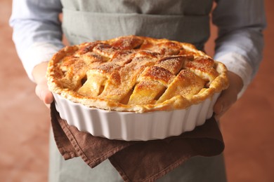 Photo of Woman holding tasty homemade apple pie on light coral background, closeup