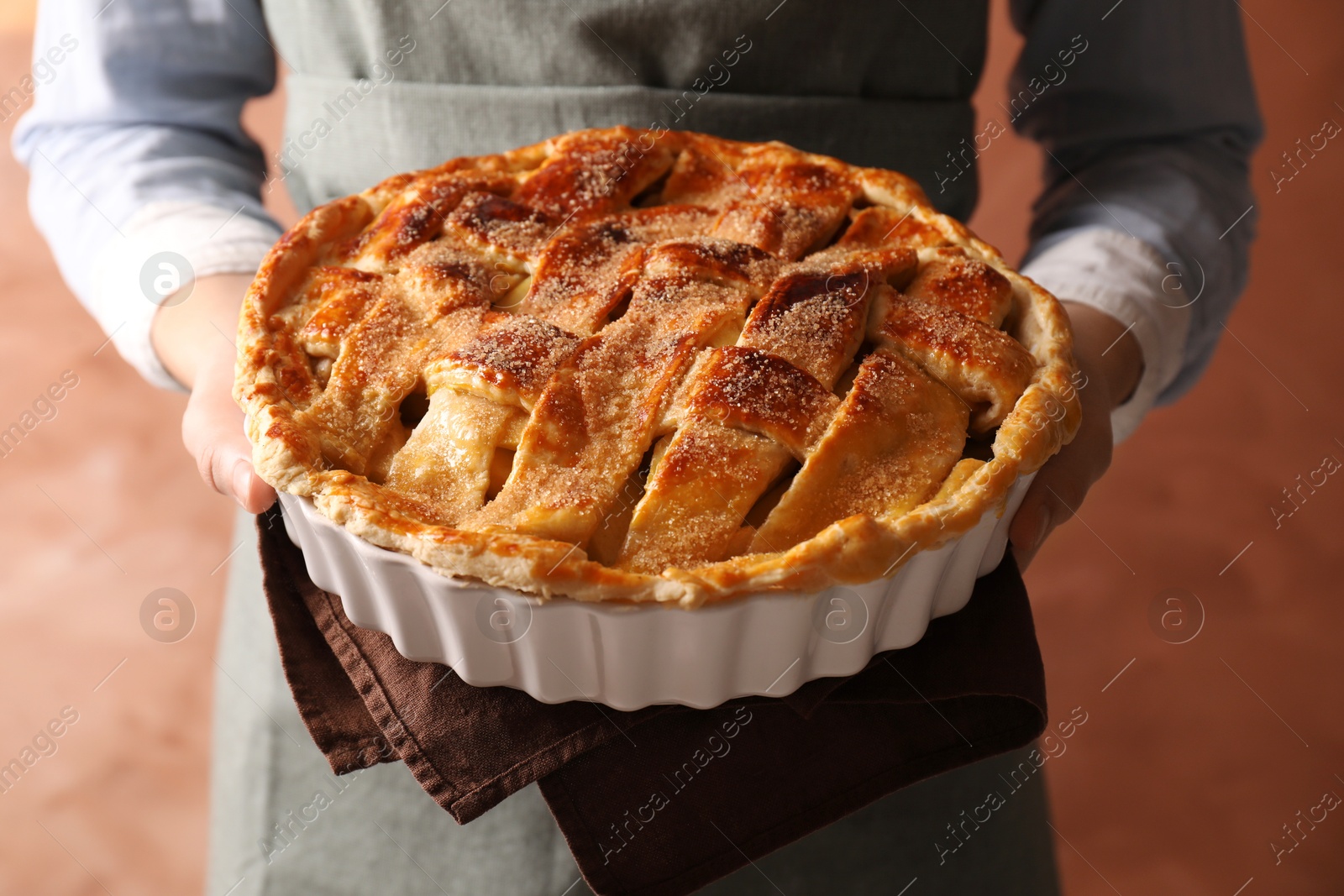 Photo of Woman holding tasty homemade apple pie on light coral background, closeup