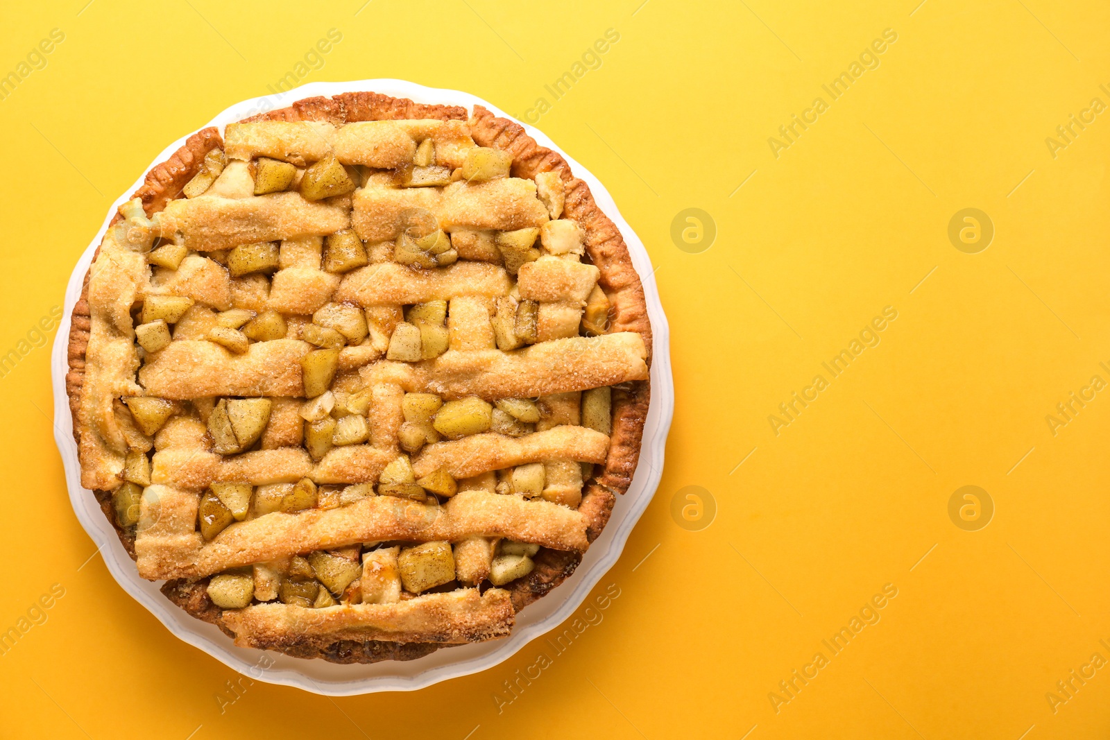 Photo of Tasty homemade apple pie on yellow background, top view. Space for text