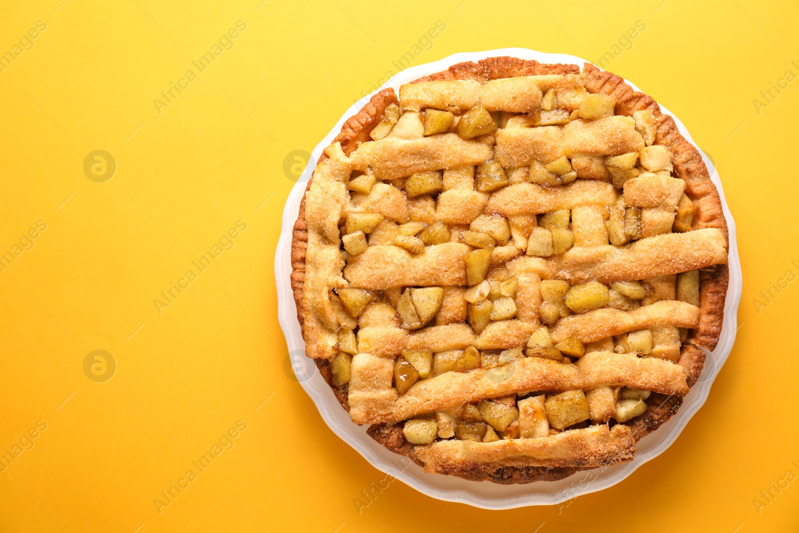 Photo of Tasty homemade apple pie on yellow background, top view. Space for text