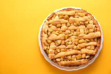 Photo of Tasty homemade apple pie on yellow background, top view. Space for text