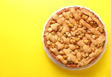 Photo of Tasty homemade apple pie on yellow background, top view. Space for text