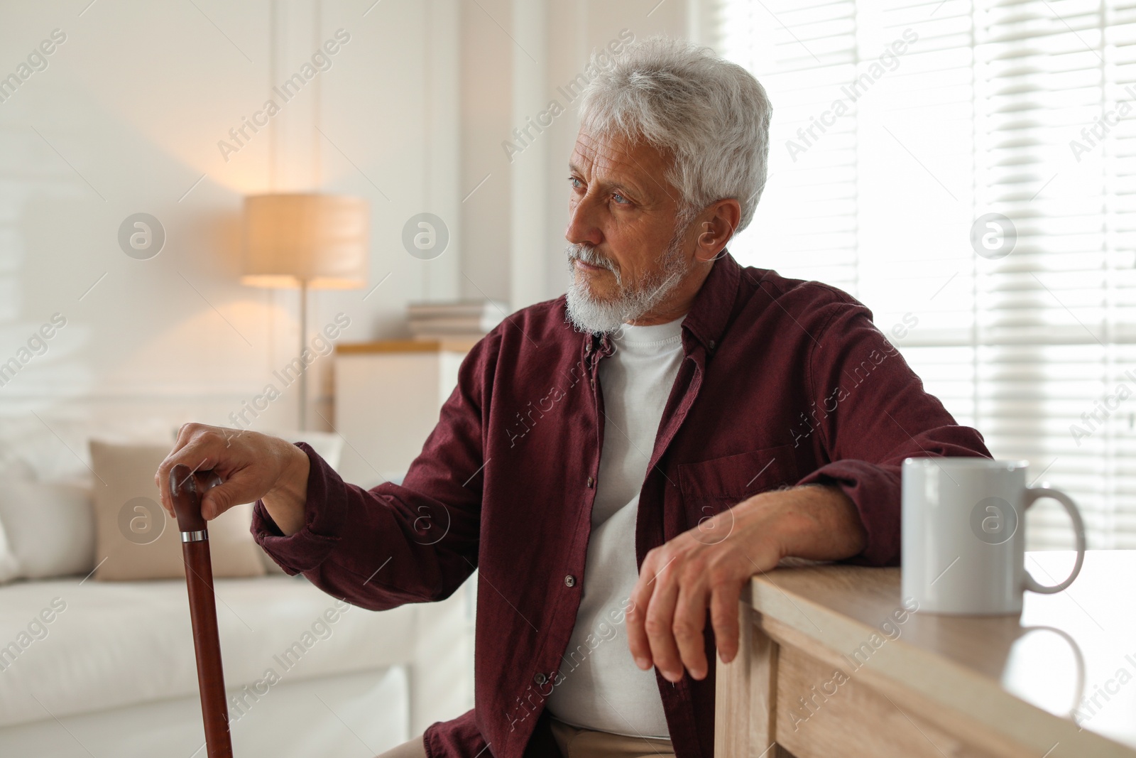 Photo of Lonely senior man with walking cane sitting at table in room