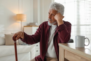 Photo of Lonely senior man with walking cane sitting at table in room