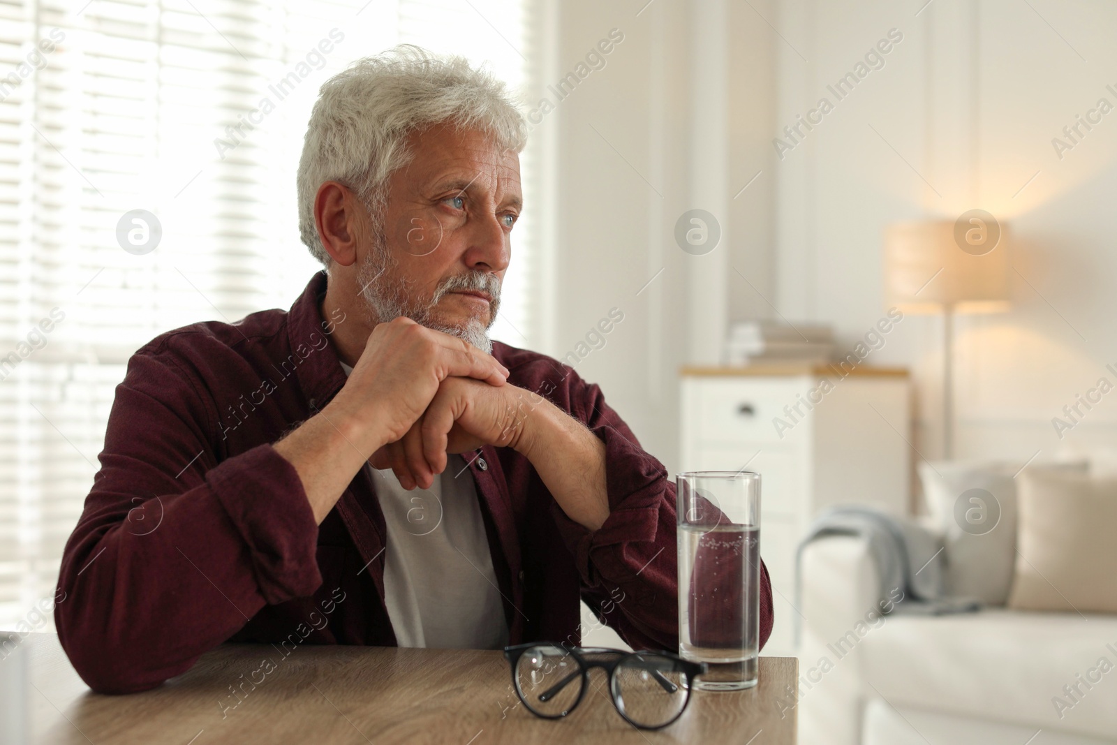 Photo of Sad senior man feeling lonely while sitting at wooden table indoors