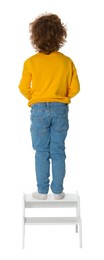 Photo of Little boy standing on step stool against white background, back view