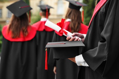 Photo of Student with graduation hat and diploma at ceremony outdoors, selective focus