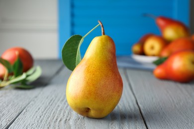 Photo of Ripe juicy pear with green leaf on grey wooden table