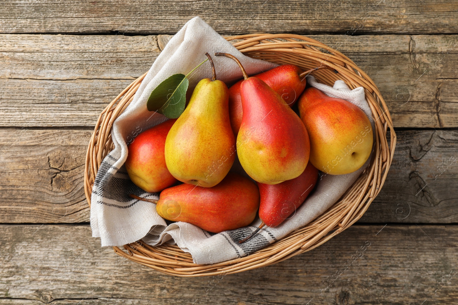 Photo of Ripe juicy pears in wicker basket on wooden table, top view