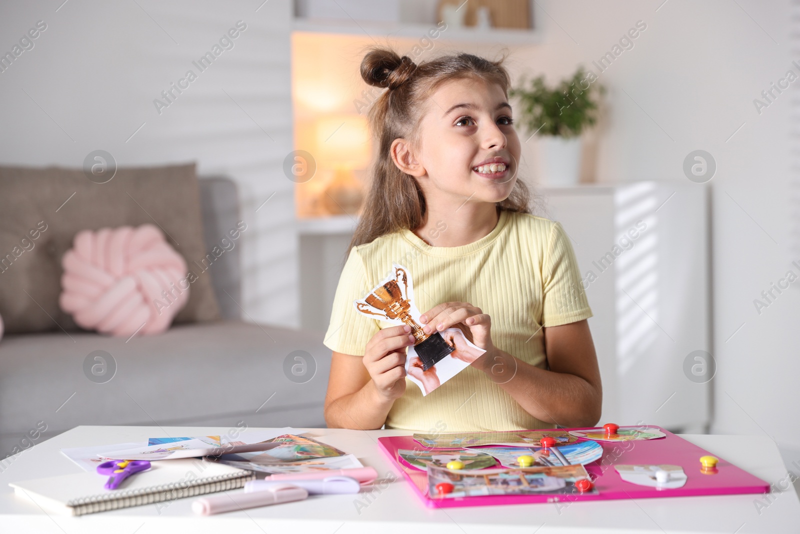 Photo of Creating vision board. Girl with picture of golden cup trophy at light table indoors