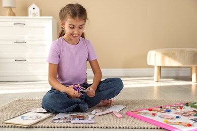 Photo of Creating vision board. Girl cutting out picture on floor indoors