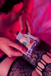 Photo of Prostitution. Woman in underwear with dollar banknotes on bed indoors, closeup