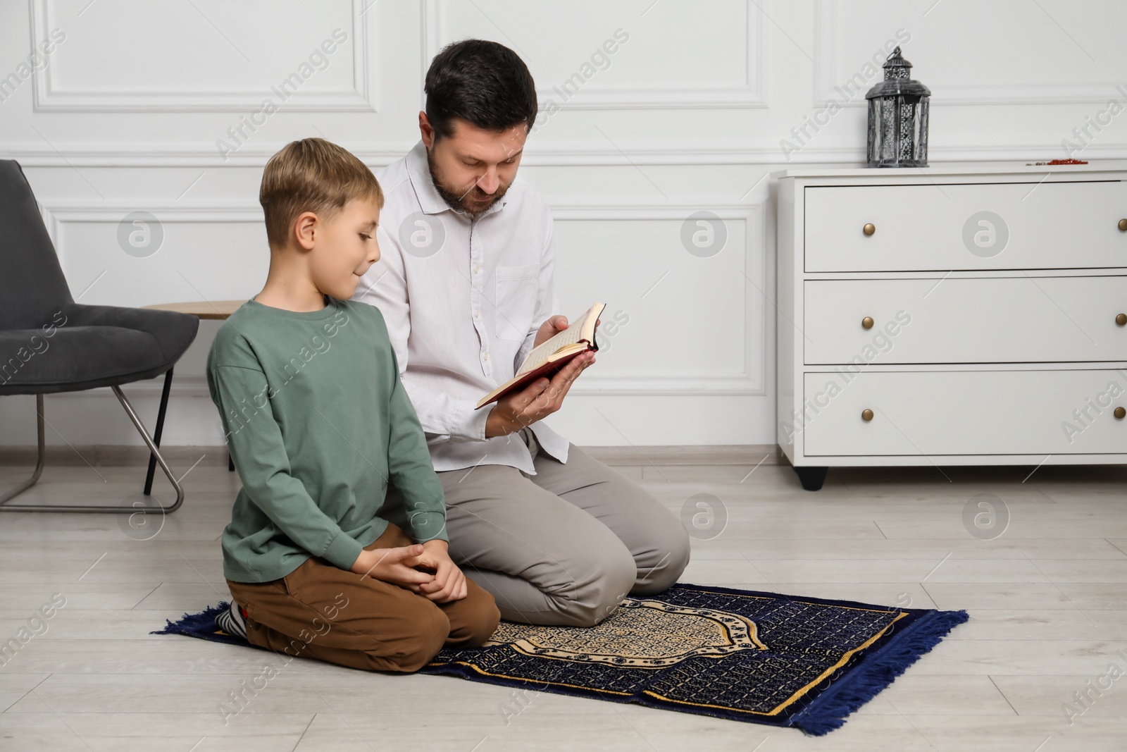 Photo of Muslim man and his son with Quran praying on mat at home