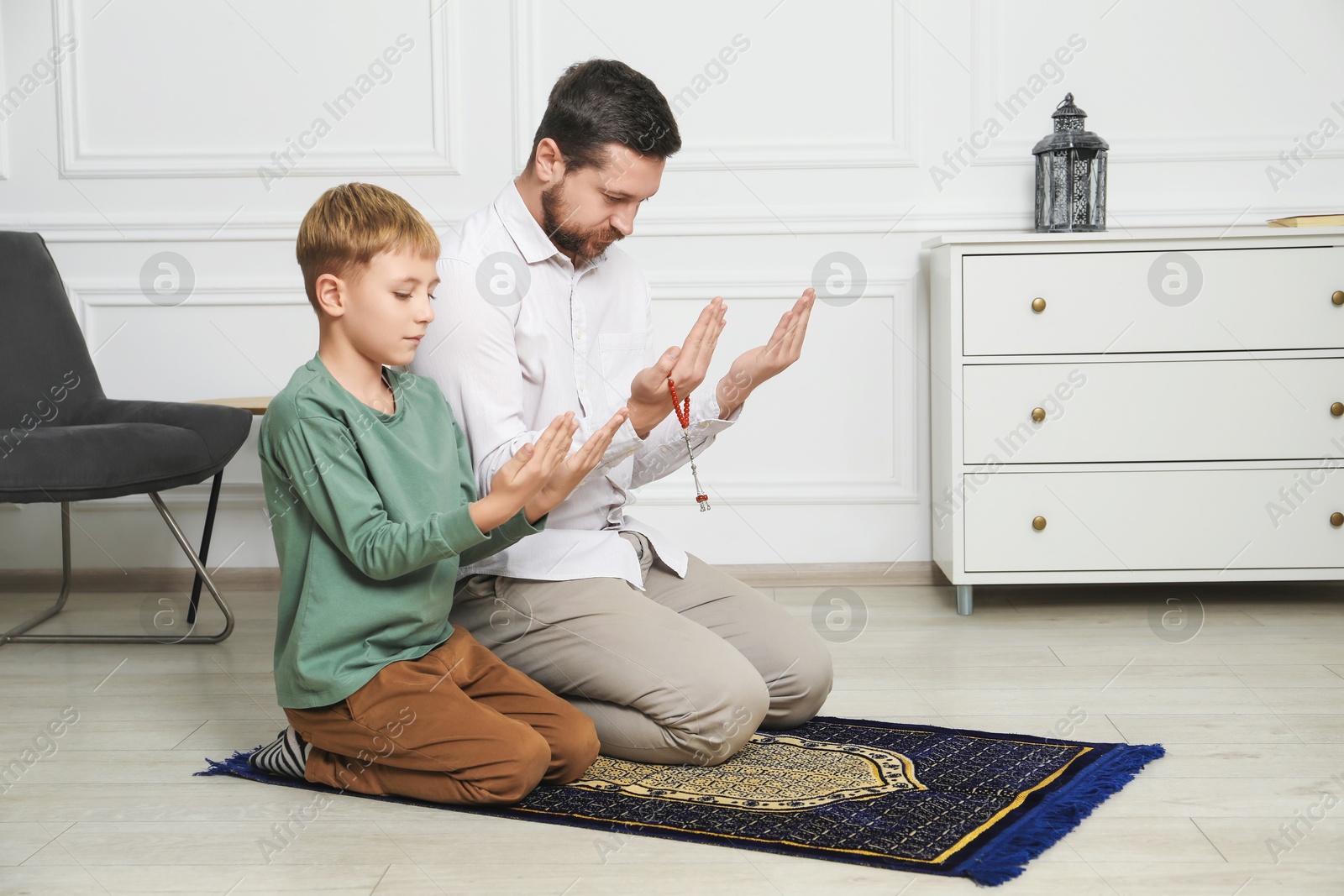 Photo of Muslim man and his son with beads praying on mat at home