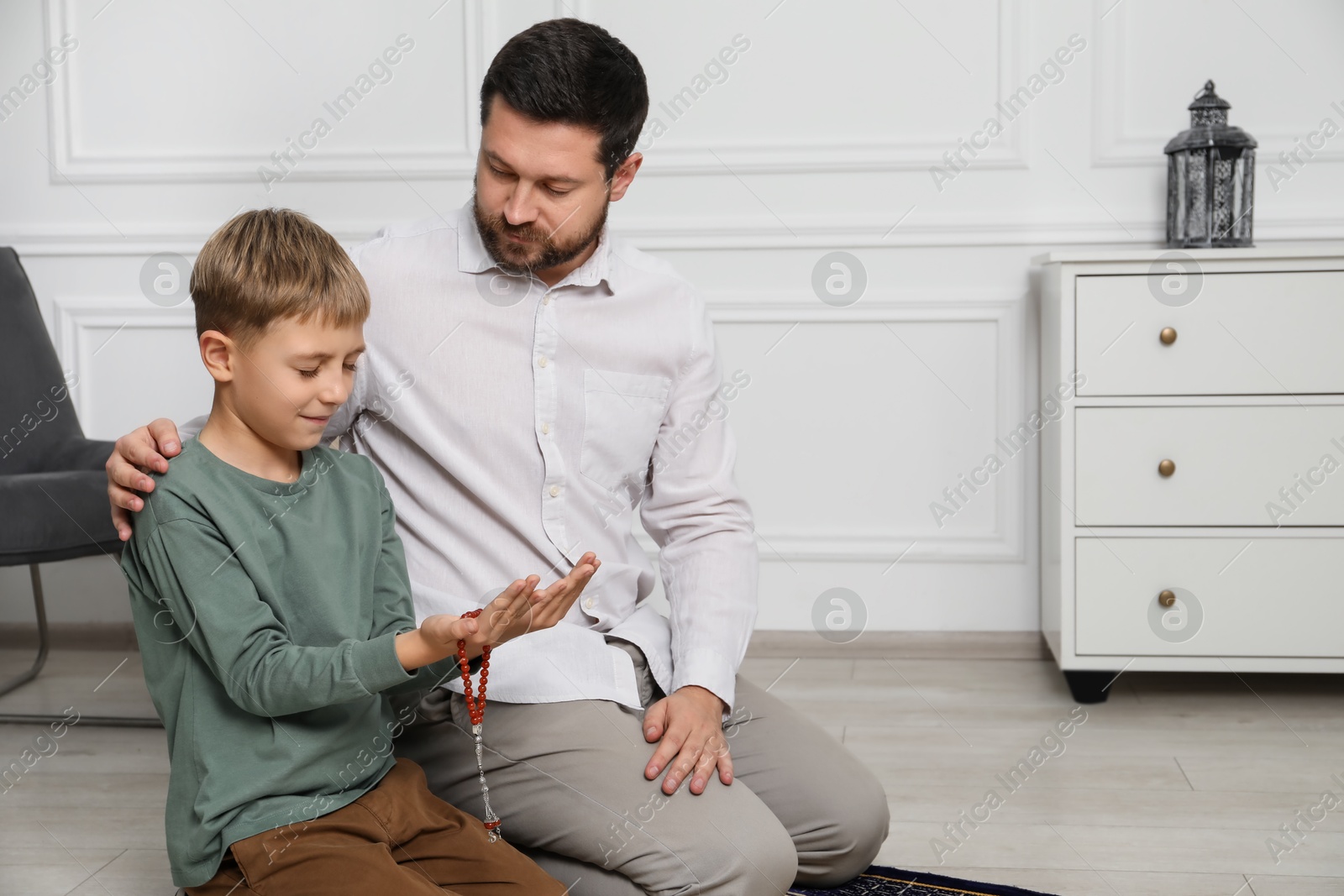 Photo of Muslim man and his son with beads praying on mat at home