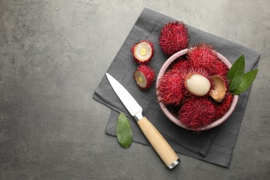 Photo of Delicious ripe rambutans, green leaves and knife on grey table, flat lay. Space for text