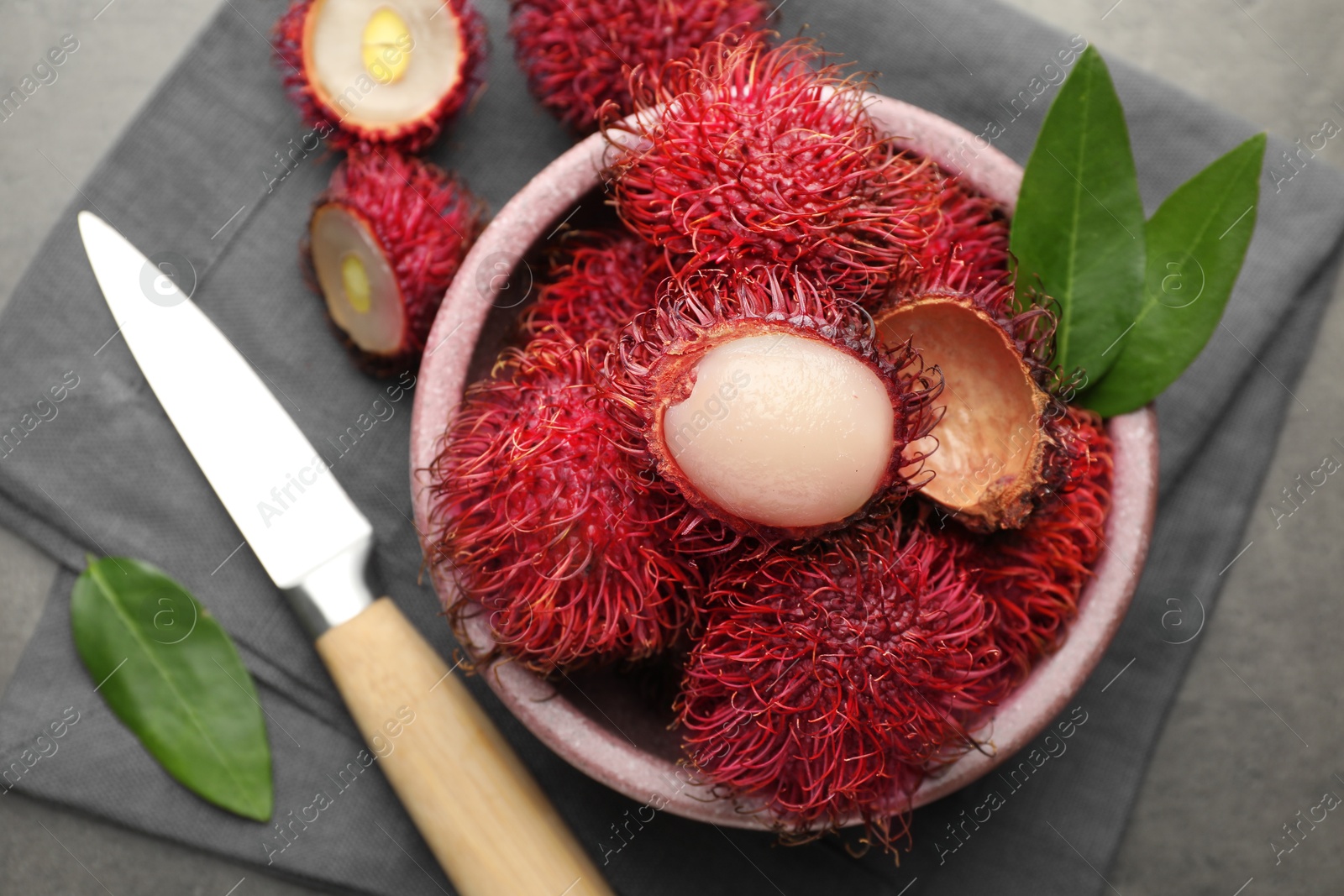 Photo of Delicious ripe rambutans, green leaves and knife on grey table, flat lay