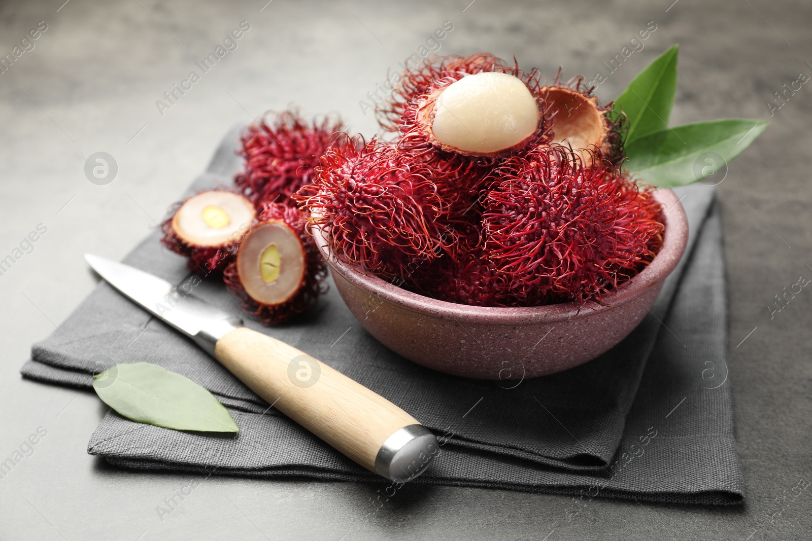 Photo of Delicious ripe rambutans, green leaves and knife on grey table, closeup