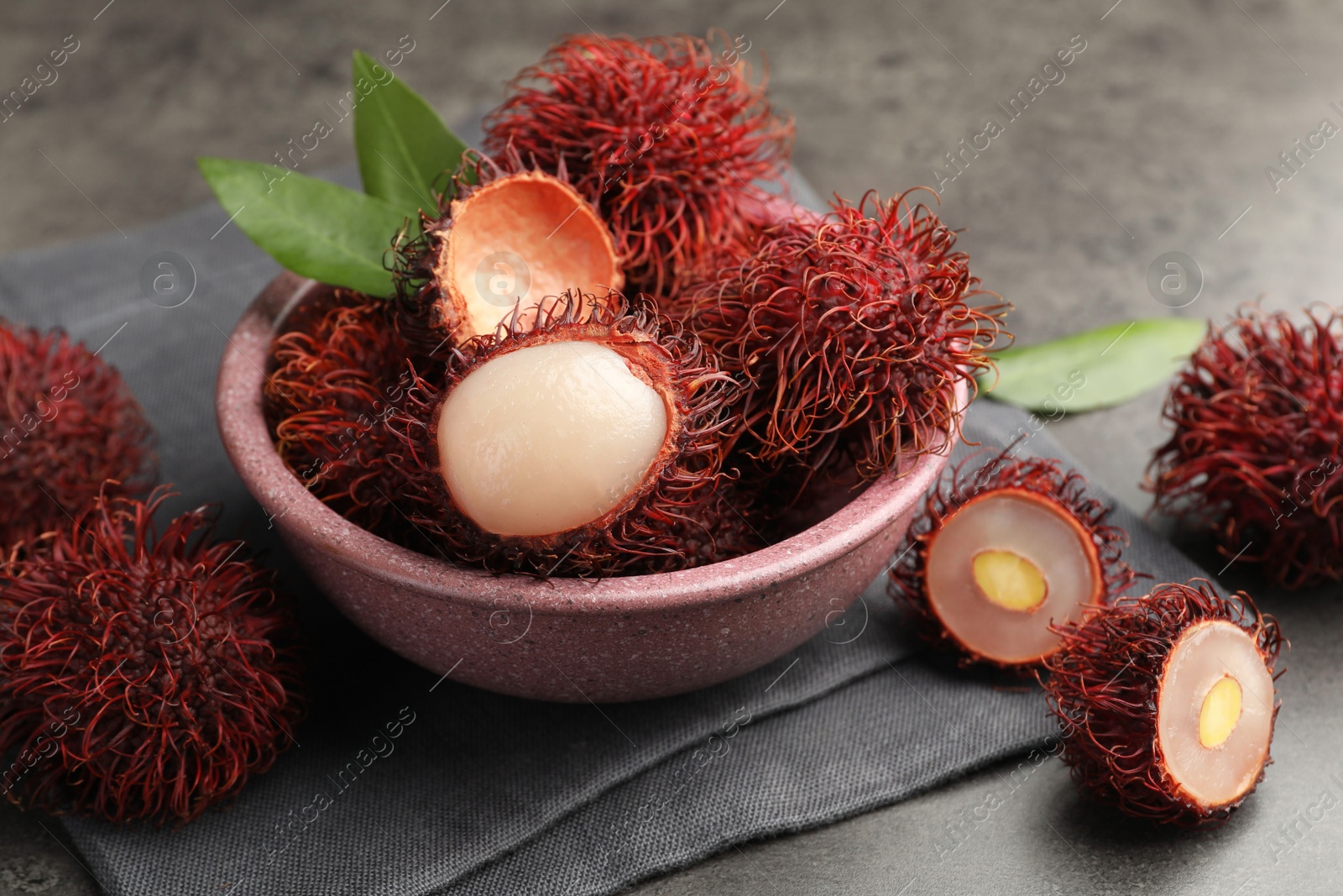 Photo of Delicious ripe rambutans and green leaves on grey table, closeup