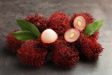 Photo of Delicious ripe rambutans and green leaves on grey table, closeup