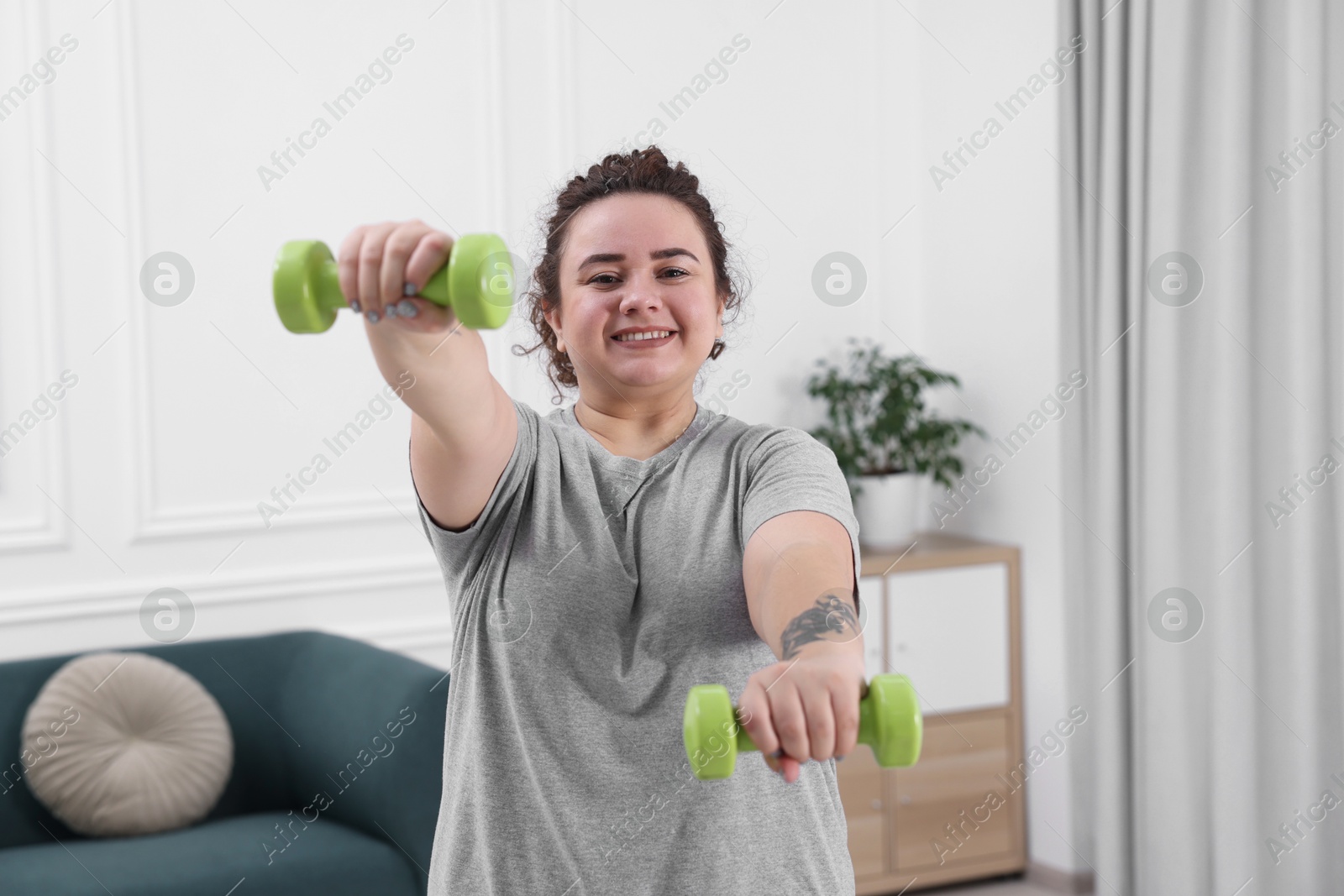 Photo of Plus size woman with dumbbells training at home