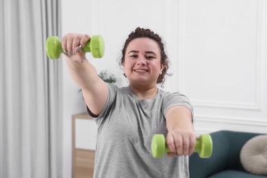 Photo of Plus size woman with dumbbells training at home