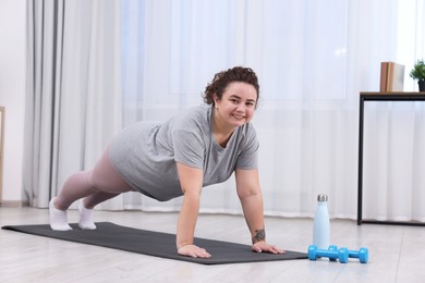 Photo of Woman doing plank exercise on fitness mat at home