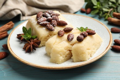 Photo of Delicious sweet semolina halva with almonds, spices and mint on light blue wooden table, closeup