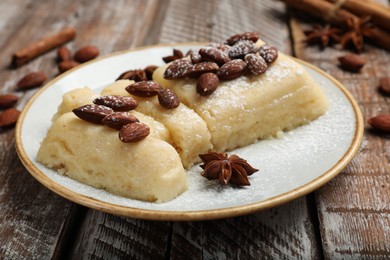 Photo of Delicious sweet semolina halva with almonds and spices on wooden table, closeup