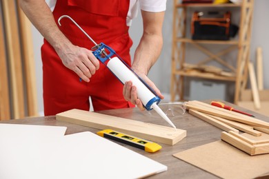 Photo of Worker with caulking gun glueing wooden plank indoors, closeup