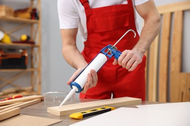 Photo of Worker with caulking gun glueing wooden plank indoors, closeup