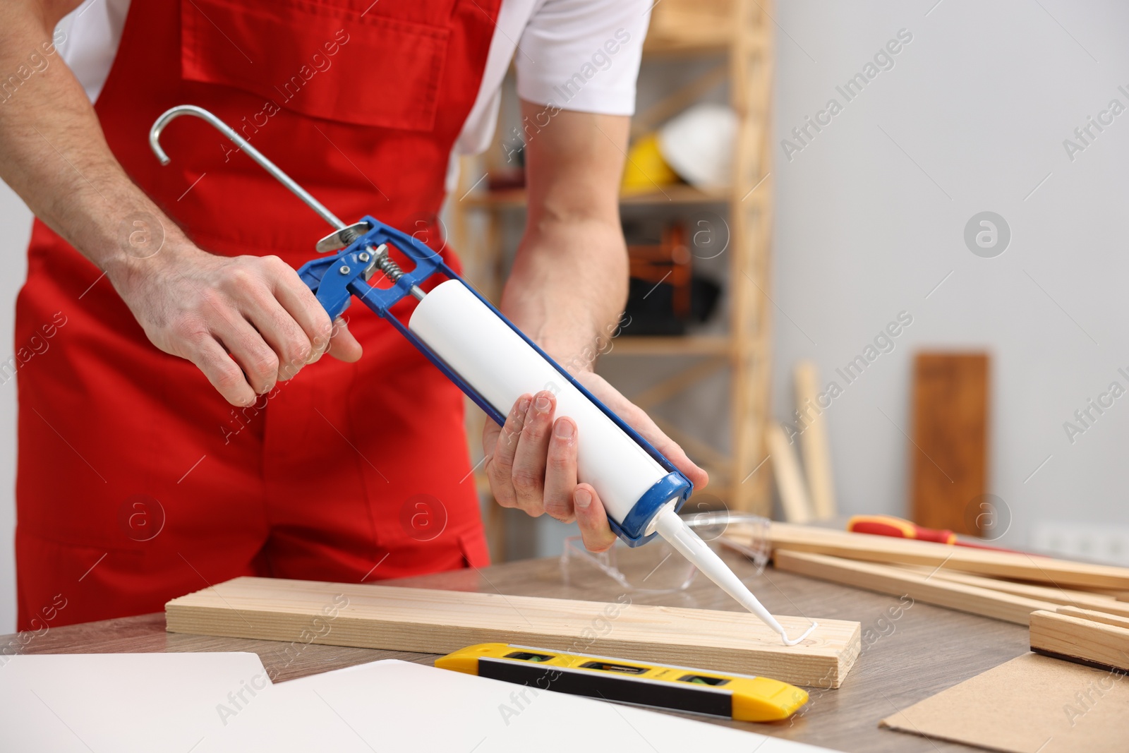 Photo of Worker with caulking gun glueing wooden plank indoors, closeup