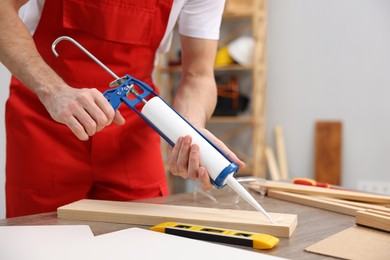 Photo of Worker with caulking gun glueing wooden plank indoors, closeup