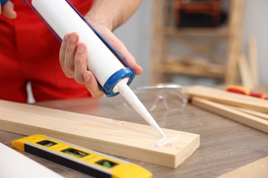 Photo of Worker with caulking gun glueing wooden plank indoors, closeup