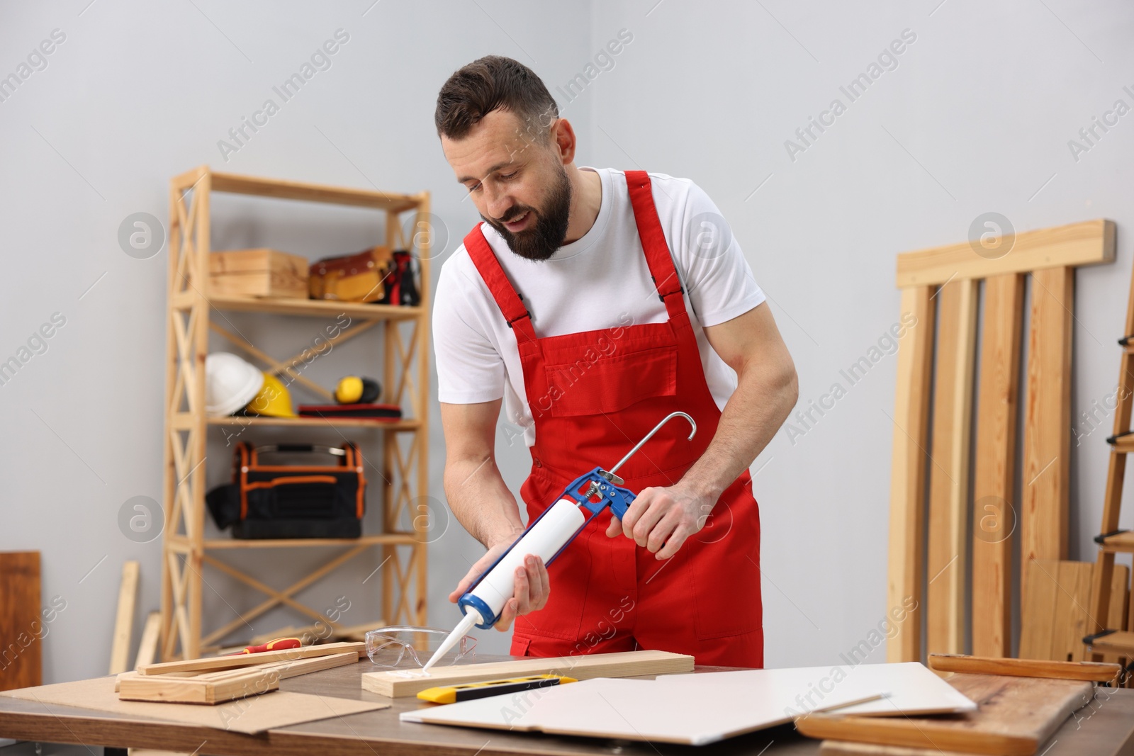 Photo of Worker with caulking gun glueing wooden plank indoors